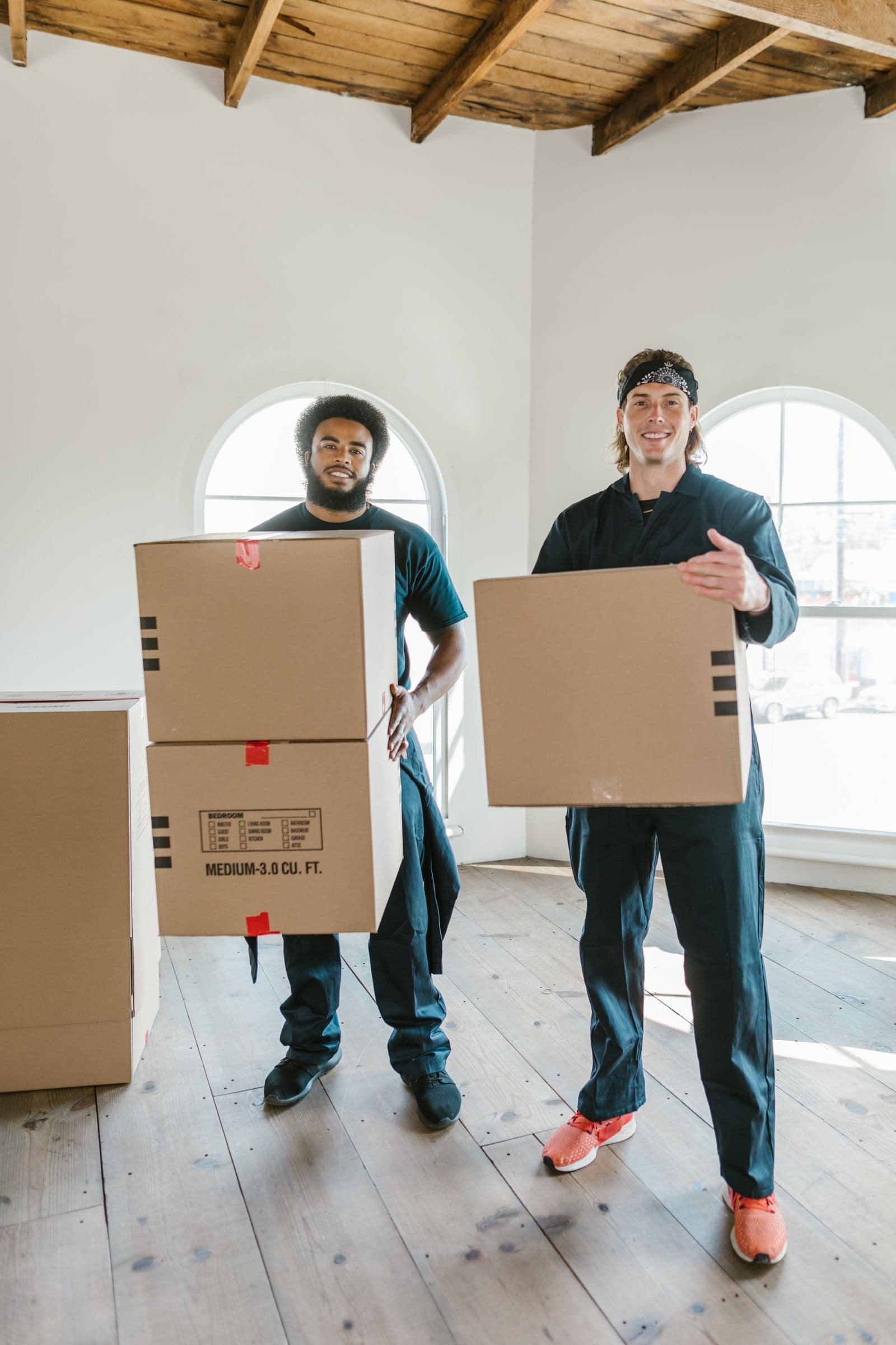 Two uniformed movers carrying packed cardboard boxes on moving day